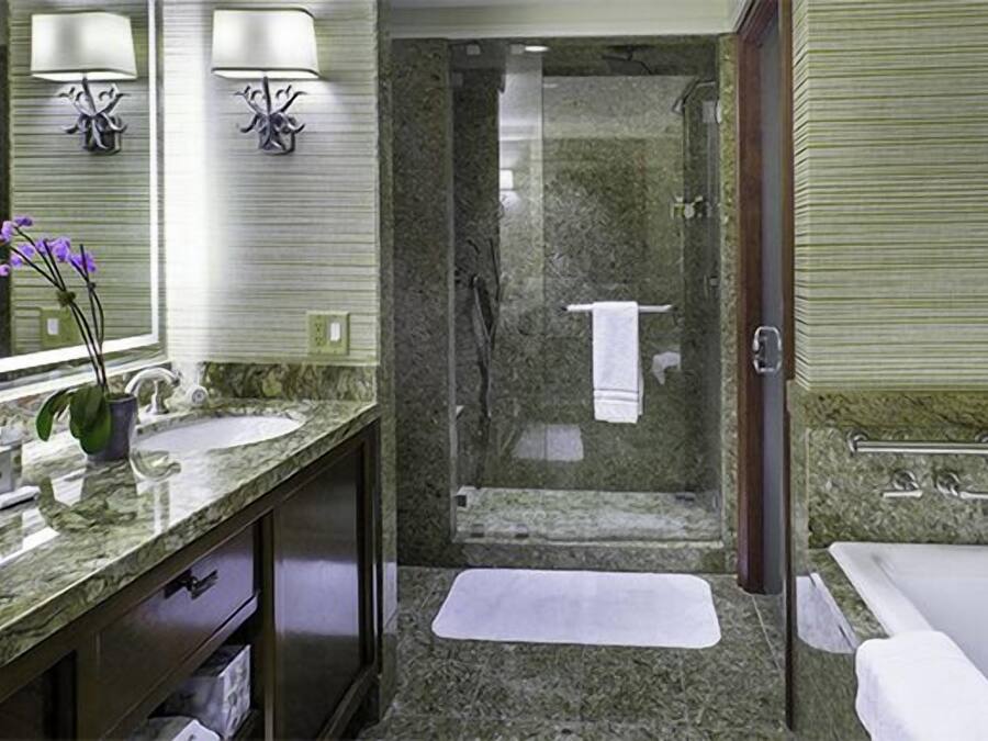 A modern bathroom with a granite countertop, a large mirror, two wall-mounted lights, a shower, and a bathtub.