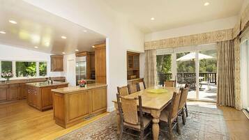 Una cocina amplia con armarios de madera y una isla grande, un comedor con mesa y sillas de madera, y vistas a un jardín exuberante a través de una puerta corrediza de vidrio.