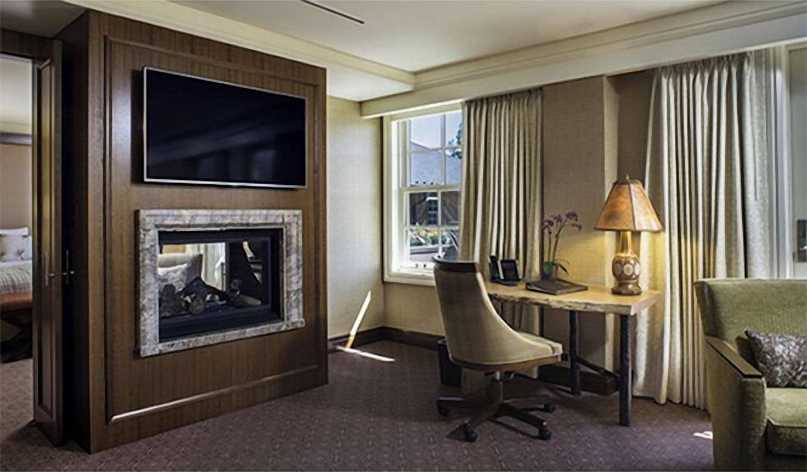 A hotel room with a flat-screen TV, a fireplace, a desk with a lamp, a chair, and a couch.