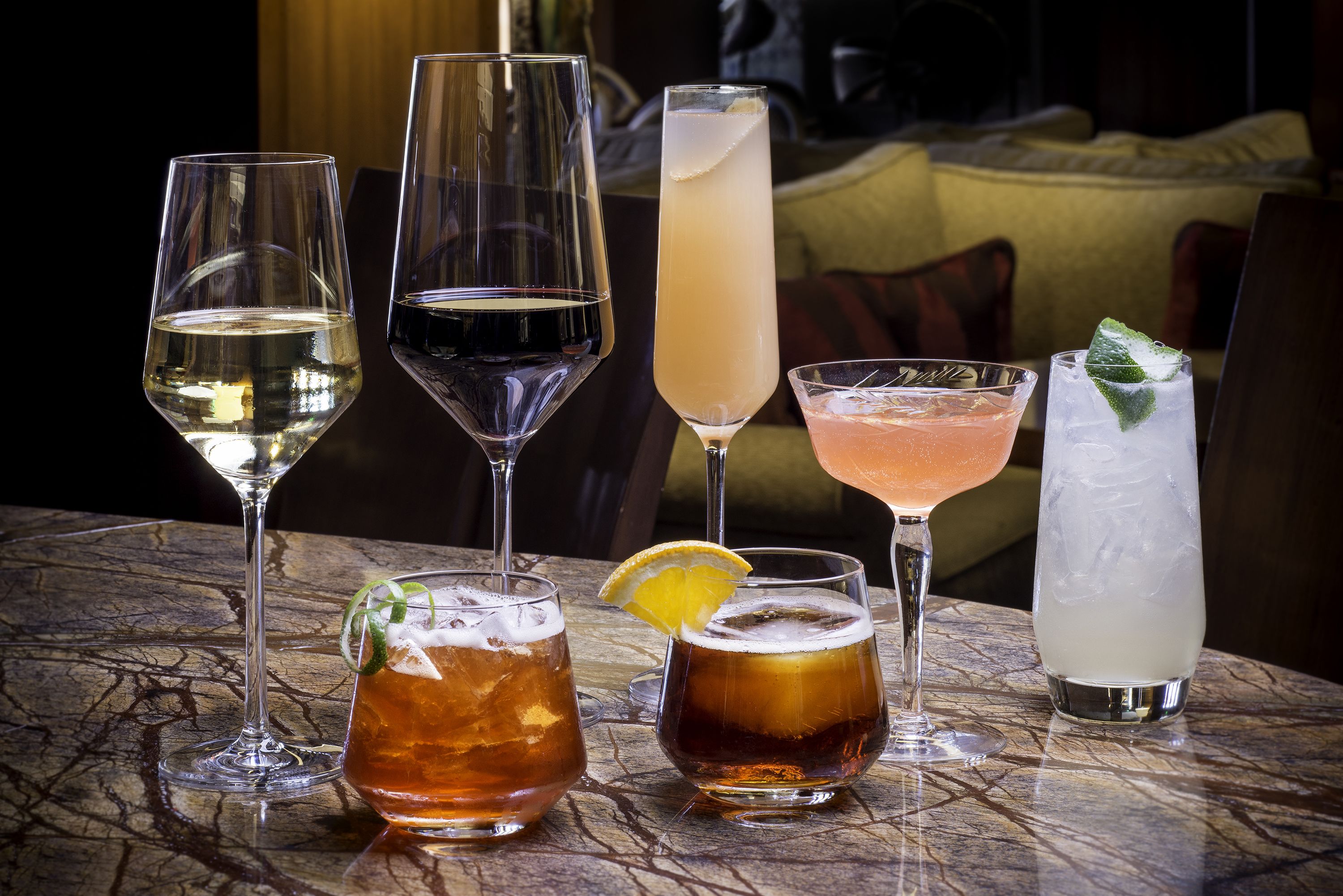 A variety of drinks on a marble table in a dimly lit room with a couch in the background.