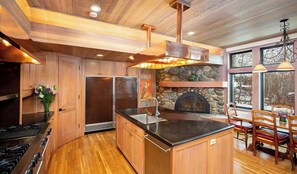 A kitchen with wooden cabinets, a stone fireplace, and a dining area with wooden chairs.