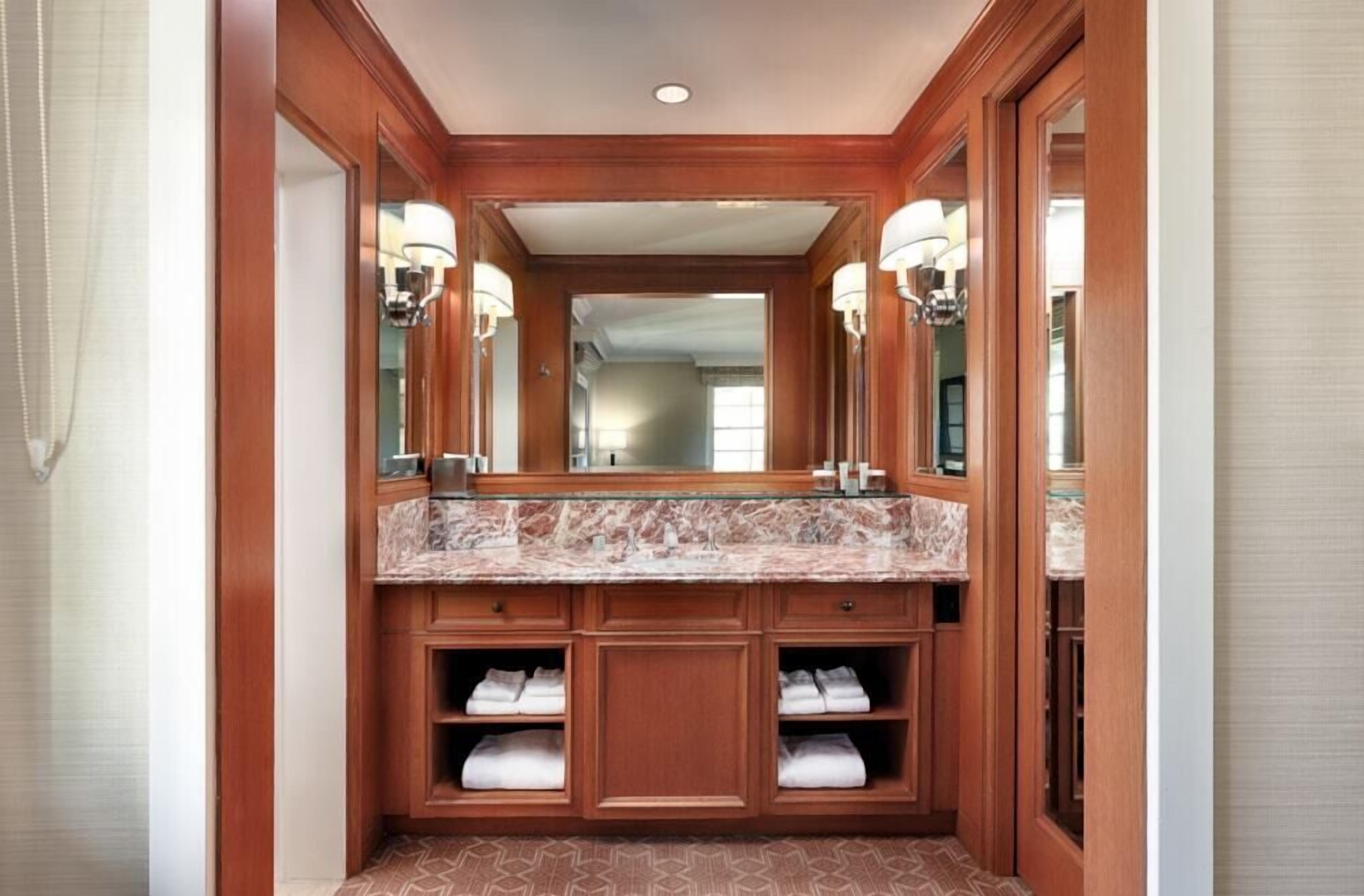 A bathroom with a marble countertop, wooden cabinetry, and built-in shelves for towels.