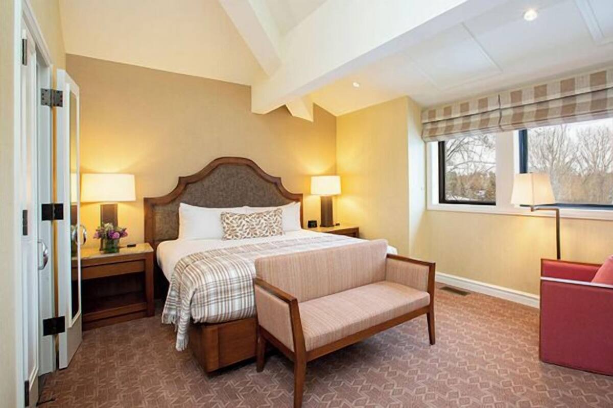 A hotel room with a bed, bedside tables, a chair, and a window with a view.