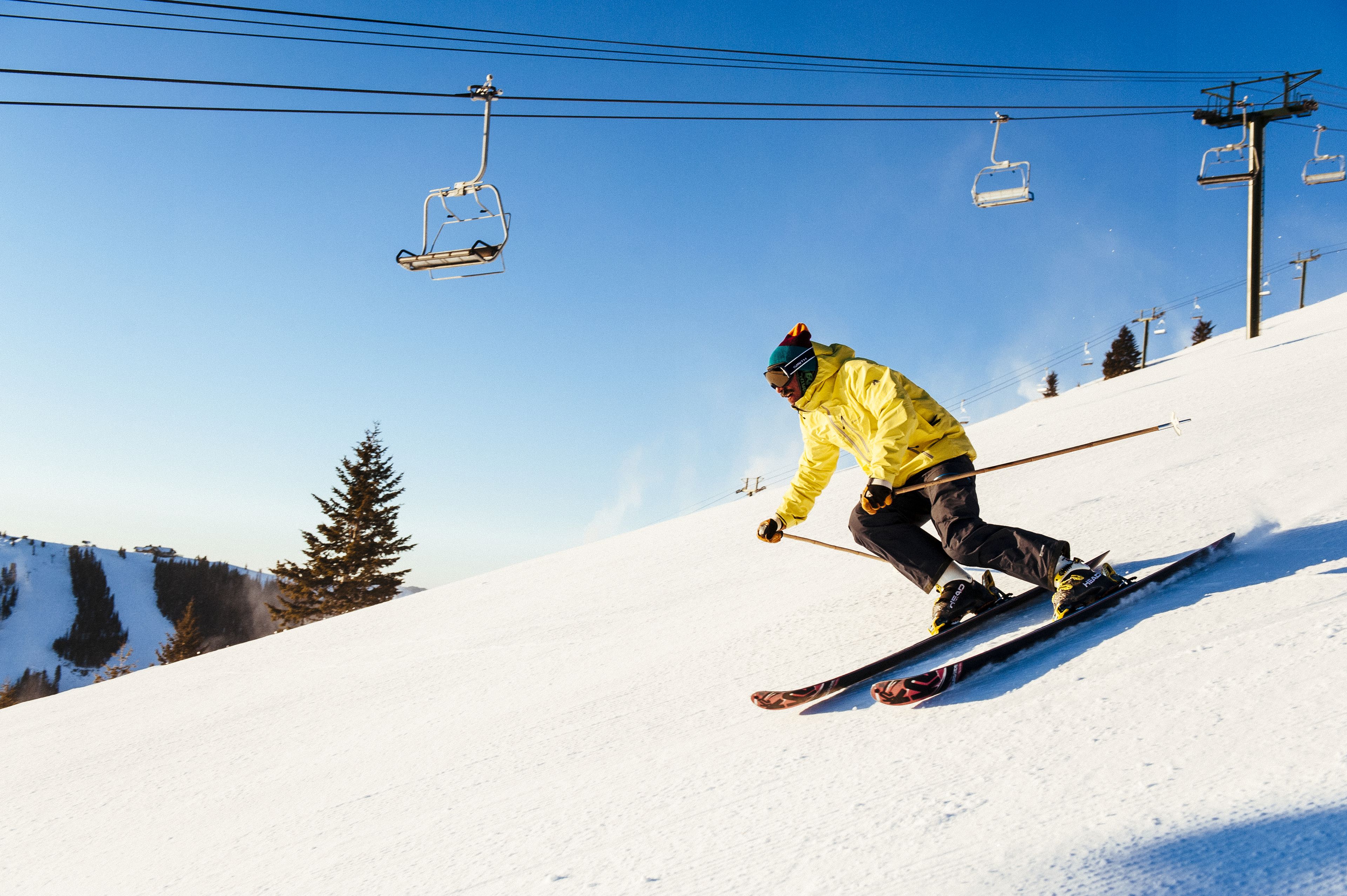 A person skiing down a snowy slope with ski lifts in the background.