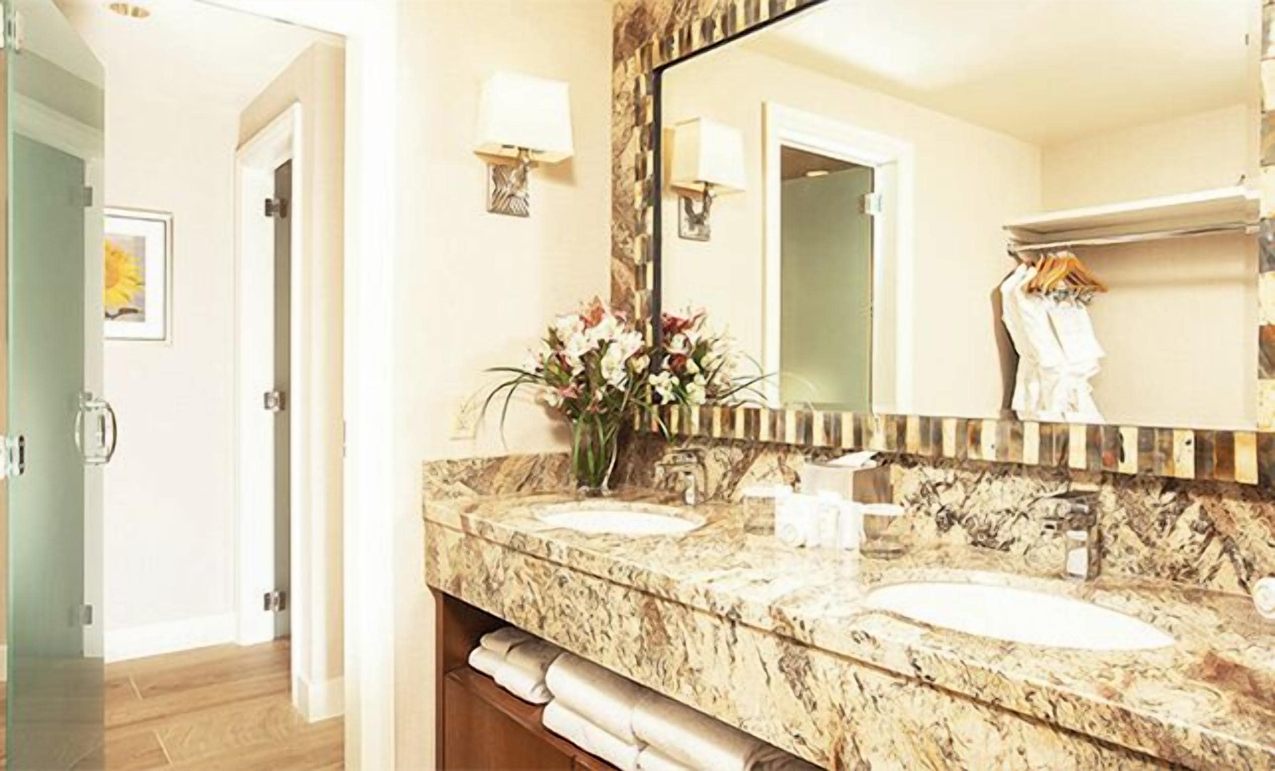 Un baño con dos lavamanos, un espejo grande y un florero con flores.