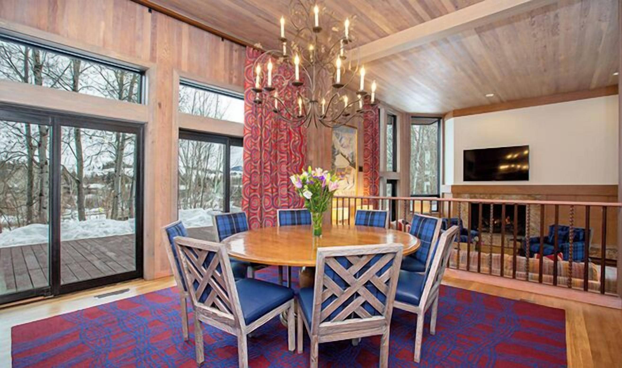 Een eetruimte met een ronde tafel, blauwe fauteuils, een kroonluchter en uitzicht op het groen.