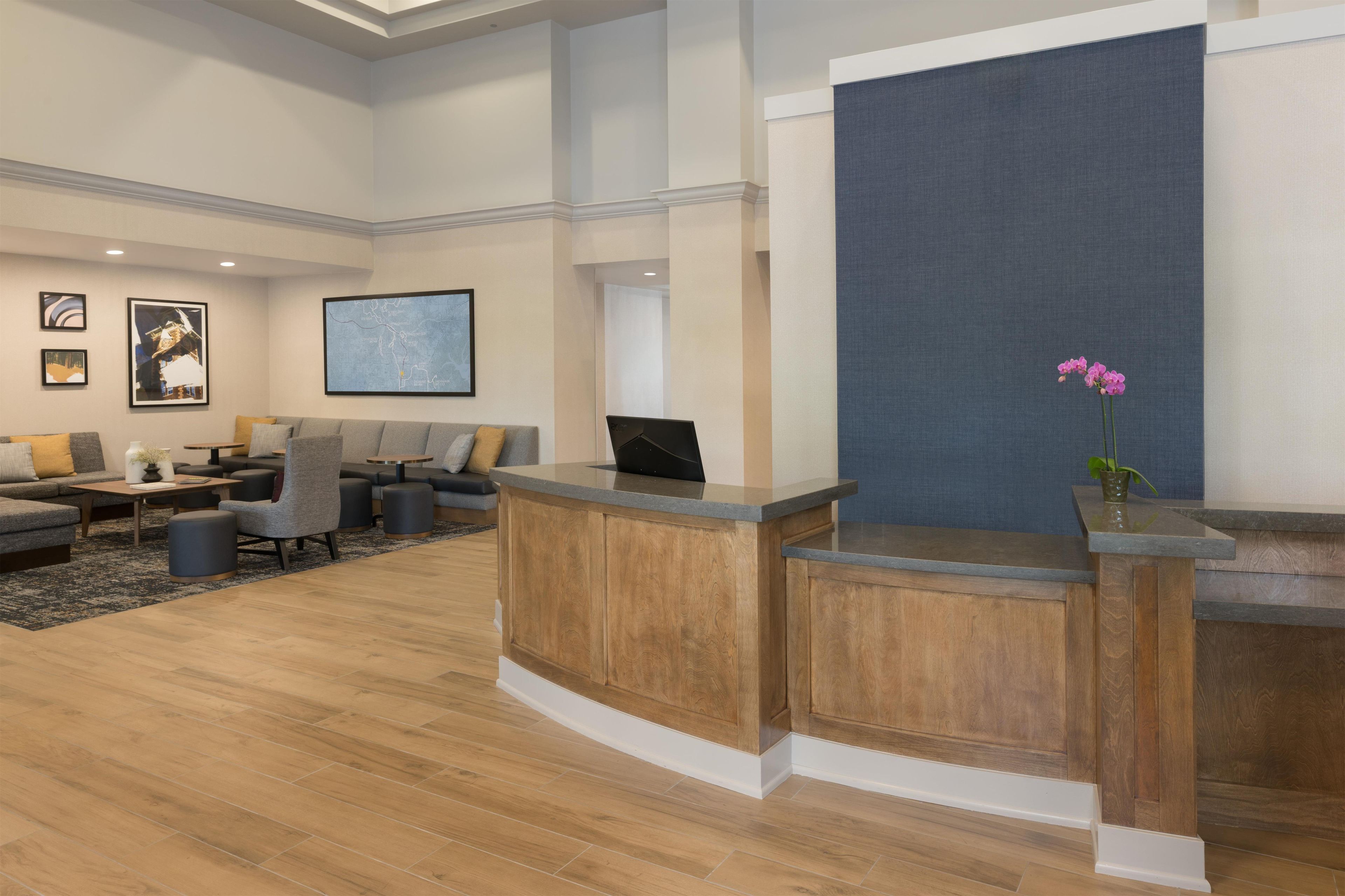A reception area with a wooden reception desk, a seating area with sofas and chairs, and a large wall-mounted screen.