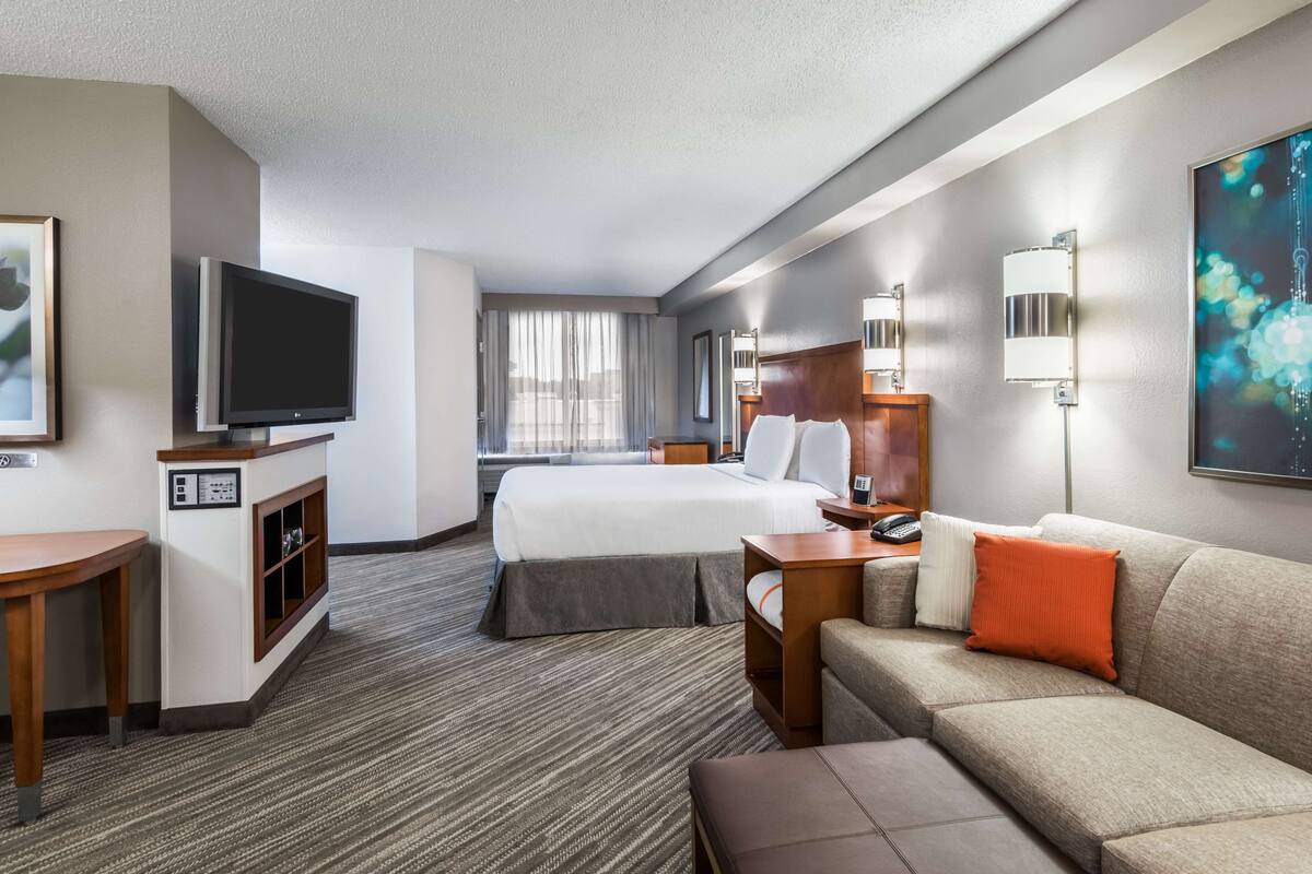 Een hotelkamer met een bed, een televisie, een bank, een bureau en een raam met gordijnen.