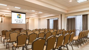 A conference room with rows of chairs, a projection screen displaying the Hyatt Place logo, and large windows with curtains.
