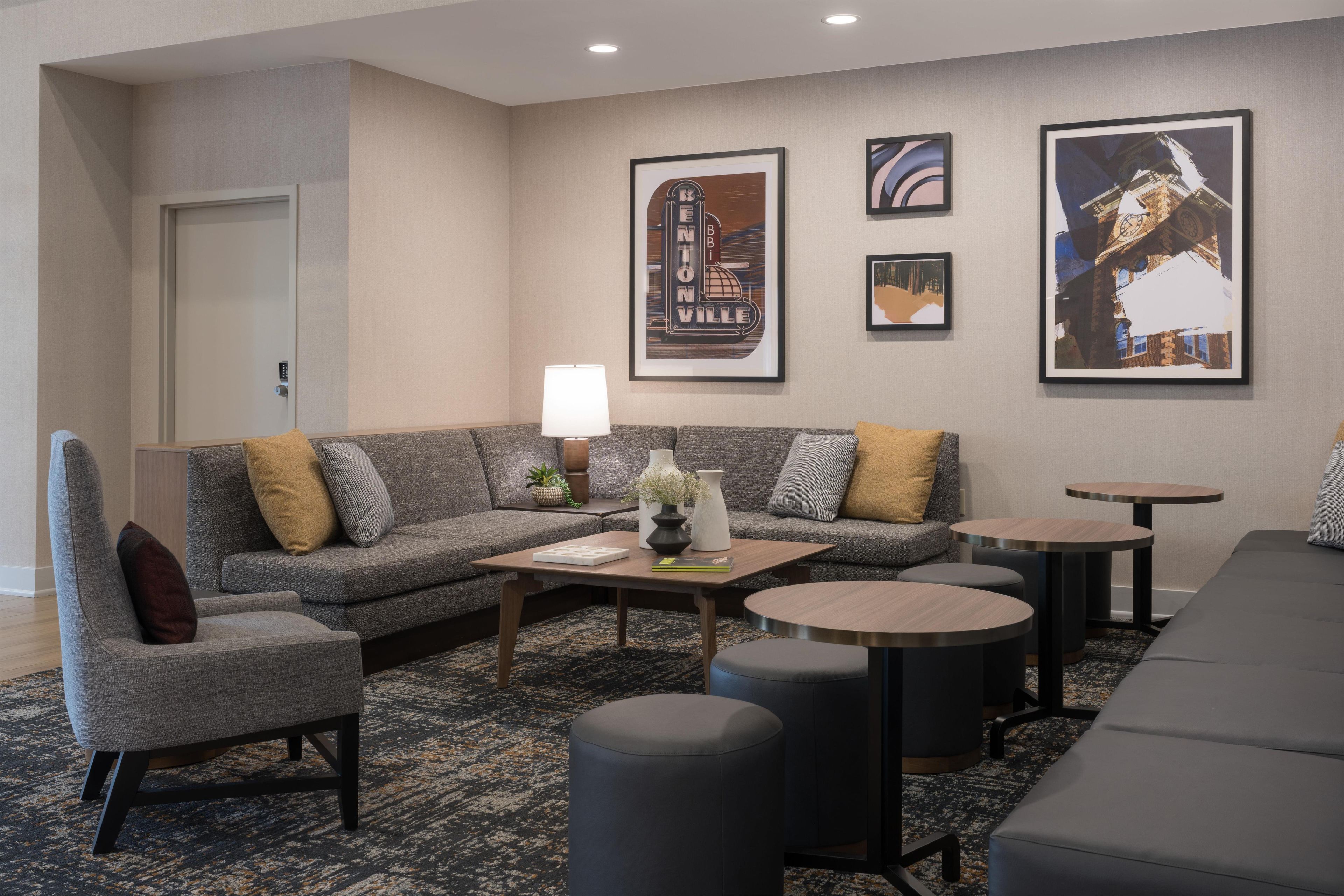 Una moderna hall d'hotel con un divano grigio, un tavolino da caffè e due tavoli rotondi.
