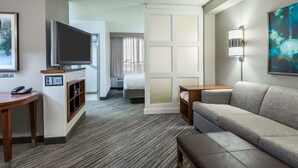 Habitación de hotel con televisión de pantalla plana, sofá, una mesita, escritorio y cama con vistas a la ciudad.