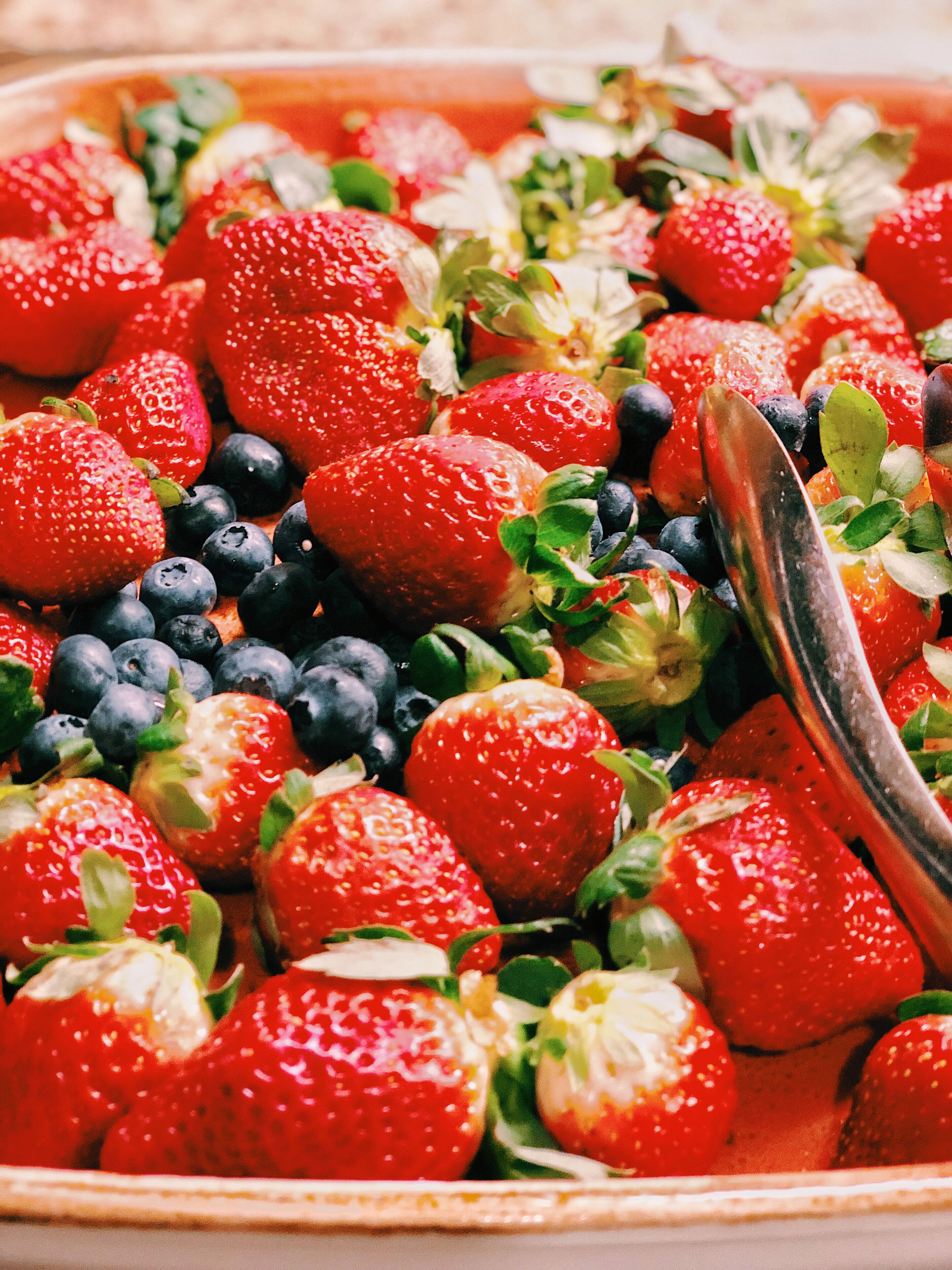 A close-up of a fruit salad with strawberries, blueberries, and green leaves.