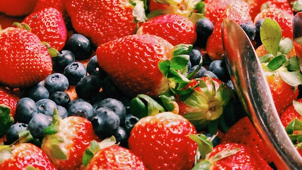 Une vue rapprochée d’une salade de fruits contenant des fraises, des myrtilles et des feuilles vertes.