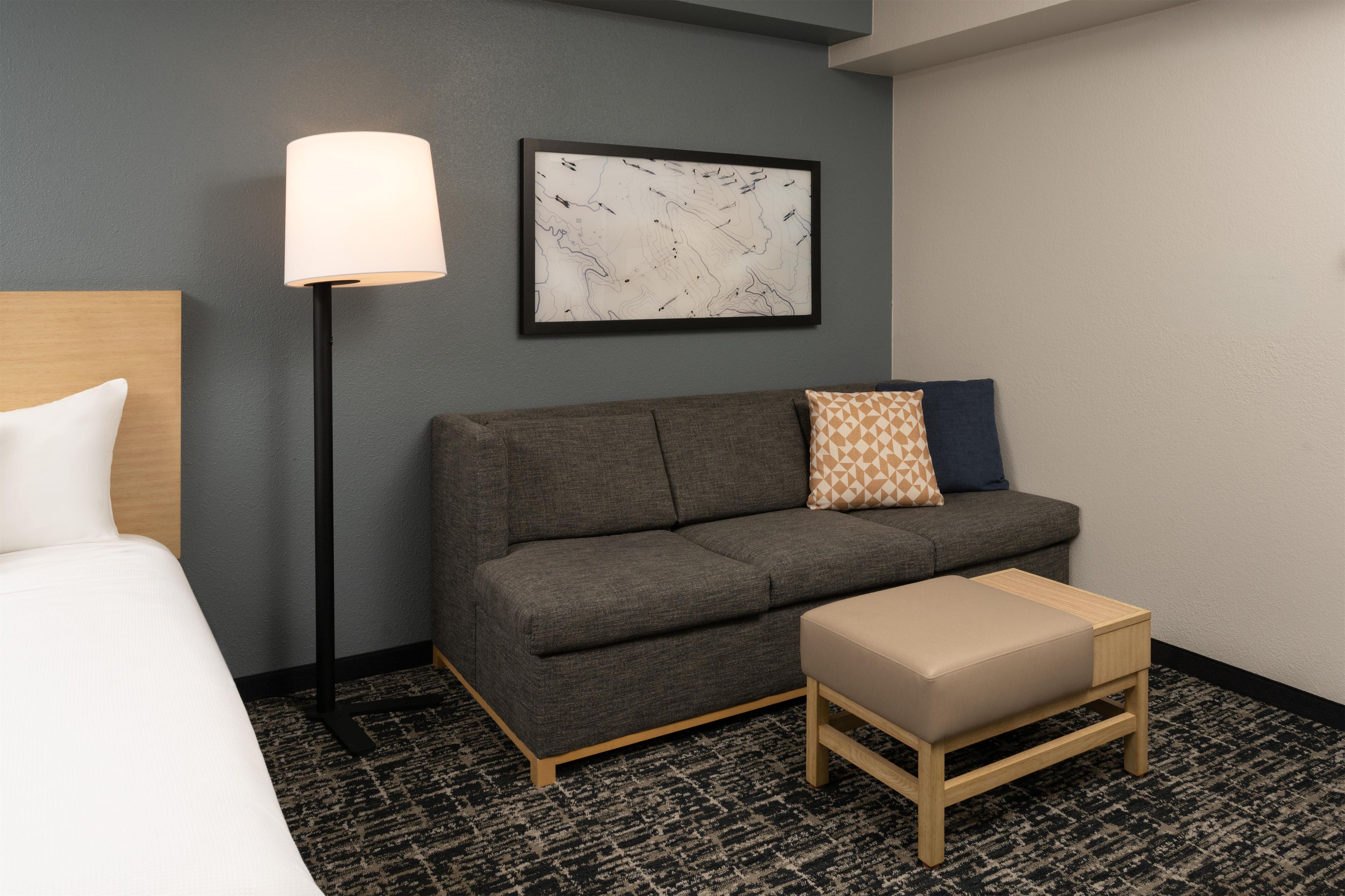Ett hotellrum med en säng, en soffa, ett litet bord, en lampa och ett konstverk som hänger på väggen.