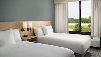 Ett hotellrum med två sängar, ett nattduksbord, en vägglampa och ett fönster med gardiner.