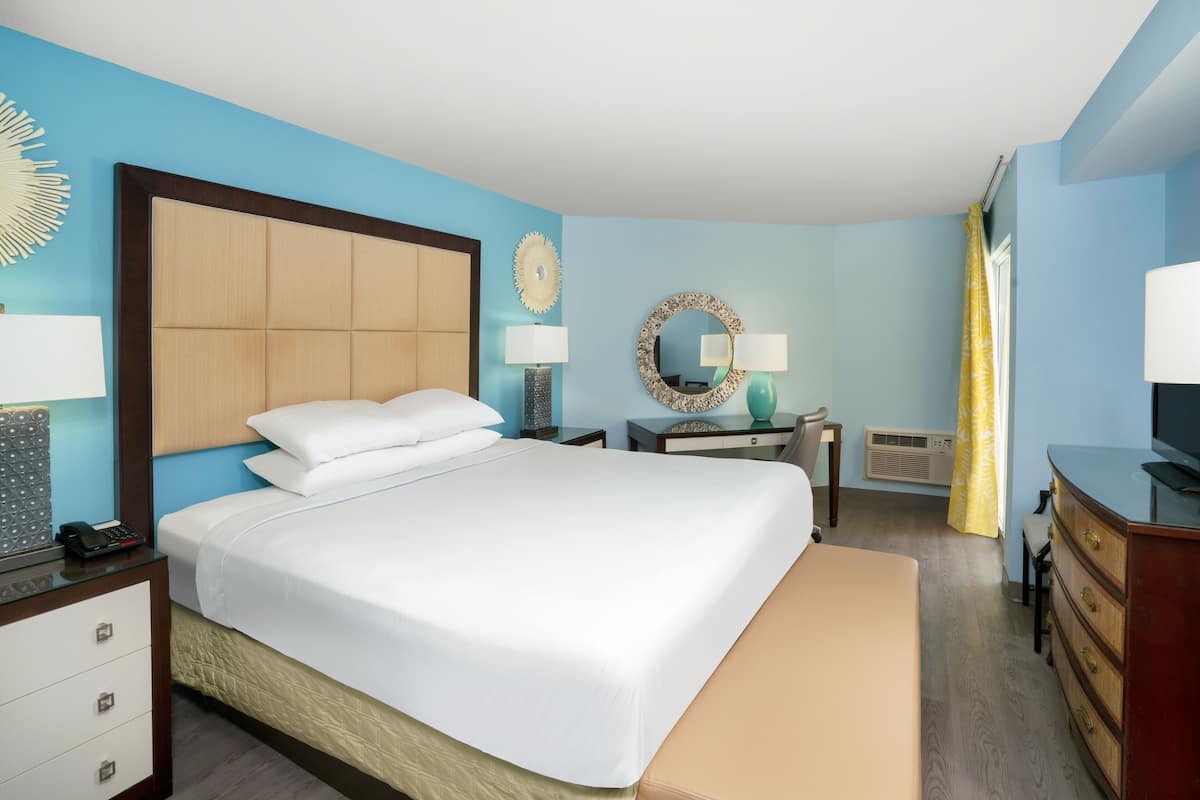 A hotel room with a large bed, bedside tables with lamps, a dresser, and a mirror.