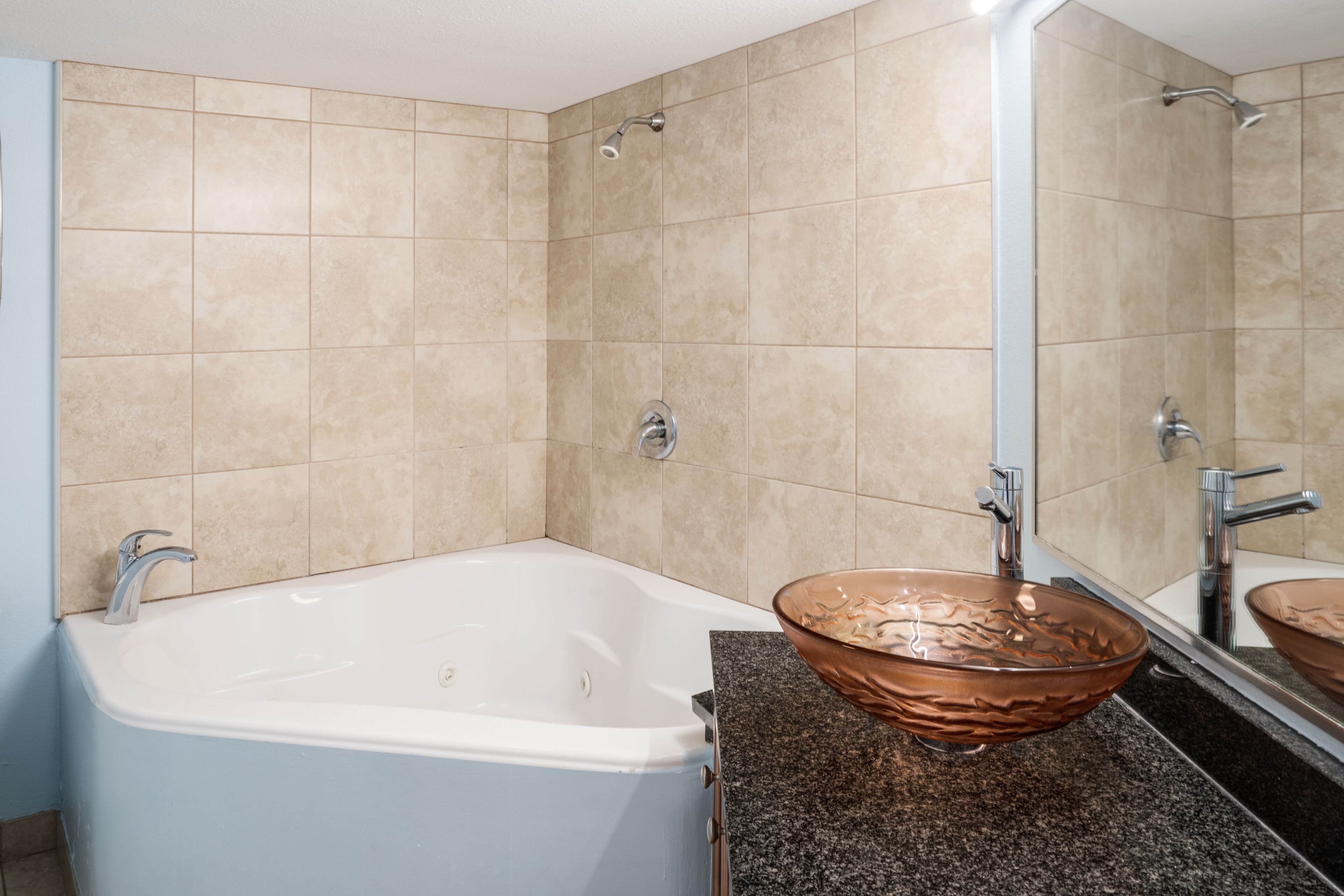 A modern bathroom with a bathtub, a copper vessel sink, and a large mirror.