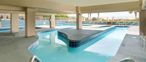 Una piscina de borde curvo, rodeada por una zona techada con pilares de concreto y piso de baldosas.