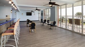 A spacious indoor area with a bar, multiple tables and chairs, ceiling fans, and large windows offering views of the outdoors. - Palette Resort Myrtle Beach (Myrtle Beach)
