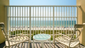 A balcony with two white chairs and a small table, overlooking a beach with people and umbrellas. - Palette Resort Myrtle Beach (Myrtle Beach)