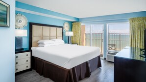 A hotel room with a large bed, a nightstand, a dresser, and a view of the outside balcony. - Palette Resort Myrtle Beach (Myrtle Beach)