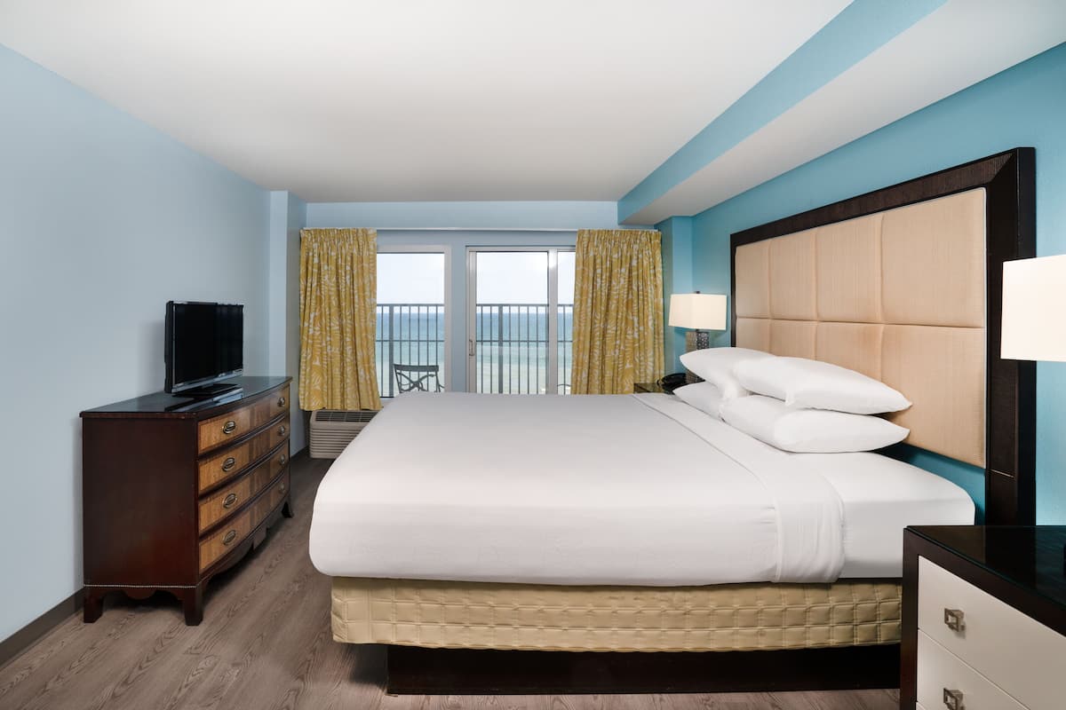 A hotel room with a large bed, a dresser, a television, and a balcony with curtains.
