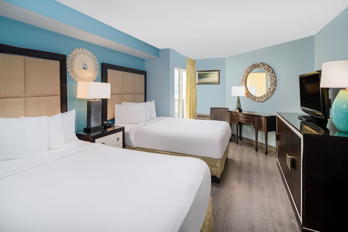 A hotel room with two beds, a desk, a television, and a mirror.
