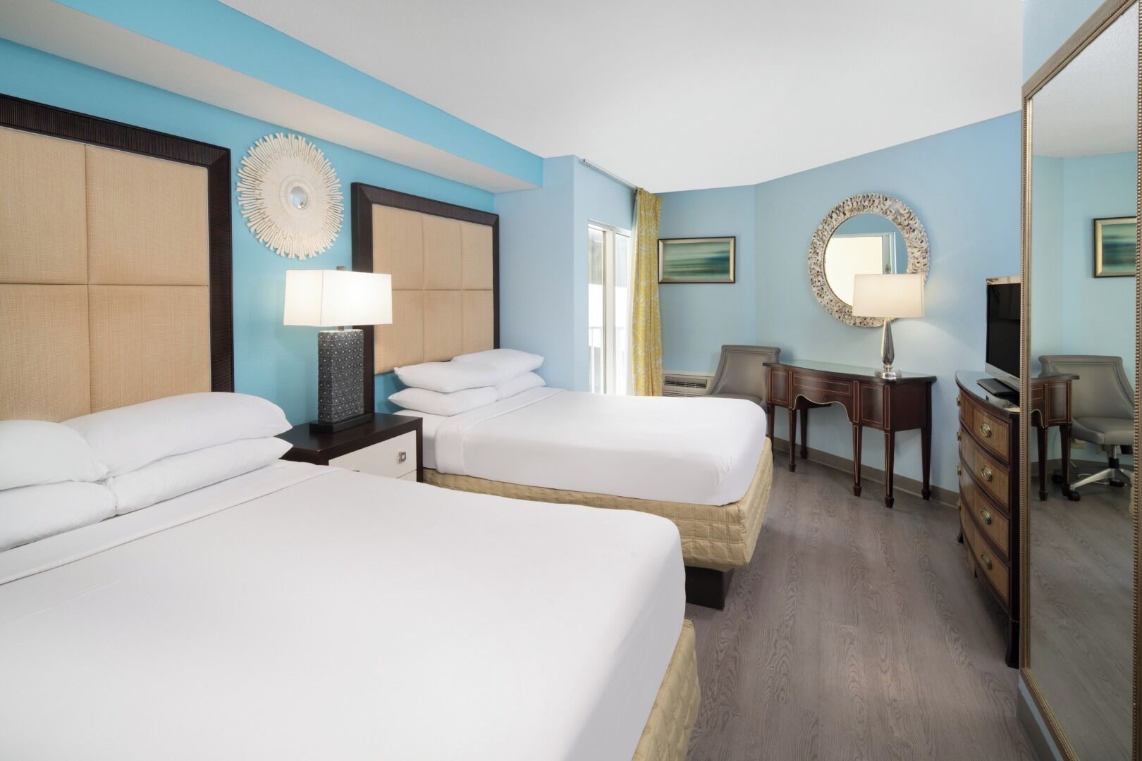 A hotel room with two beds, a desk, a chair, and a mirror.