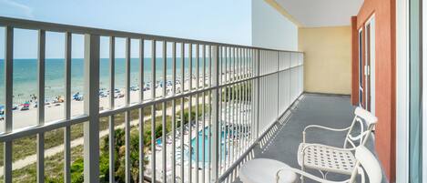 A balcony with a view of a beach and a pool.