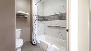 A bathroom with a toilet, a shower with a curtain, and a bathtub with a towel.