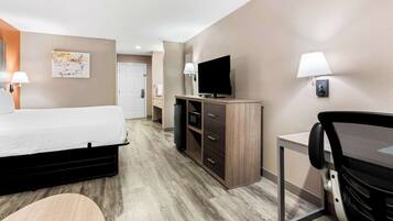 A hotel room with a bed, a desk with a television, a chair, and a lamp.