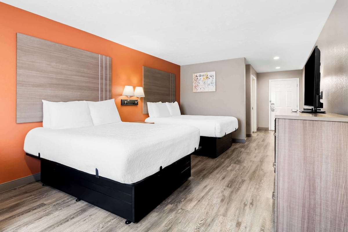 A hotel room with two beds, a desk, a TV, and a painting on the wall.