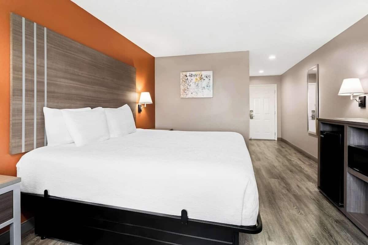 A hotel room with a bed, a nightstand, a wall-mounted lamp, a door, and a small cabinet.