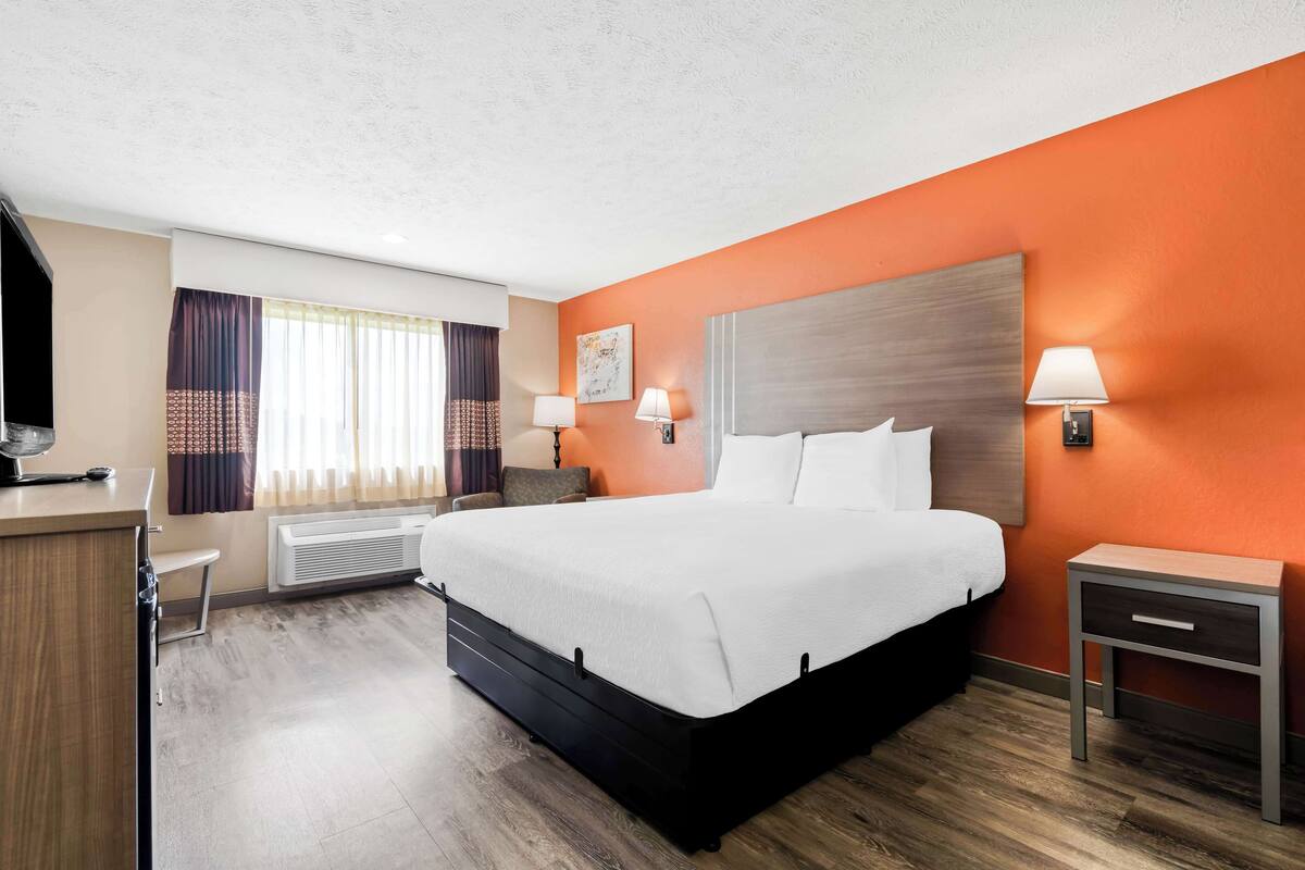 A hotel room with a large bed, two bedside tables with lamps, a desk with a chair, and a window with curtains.