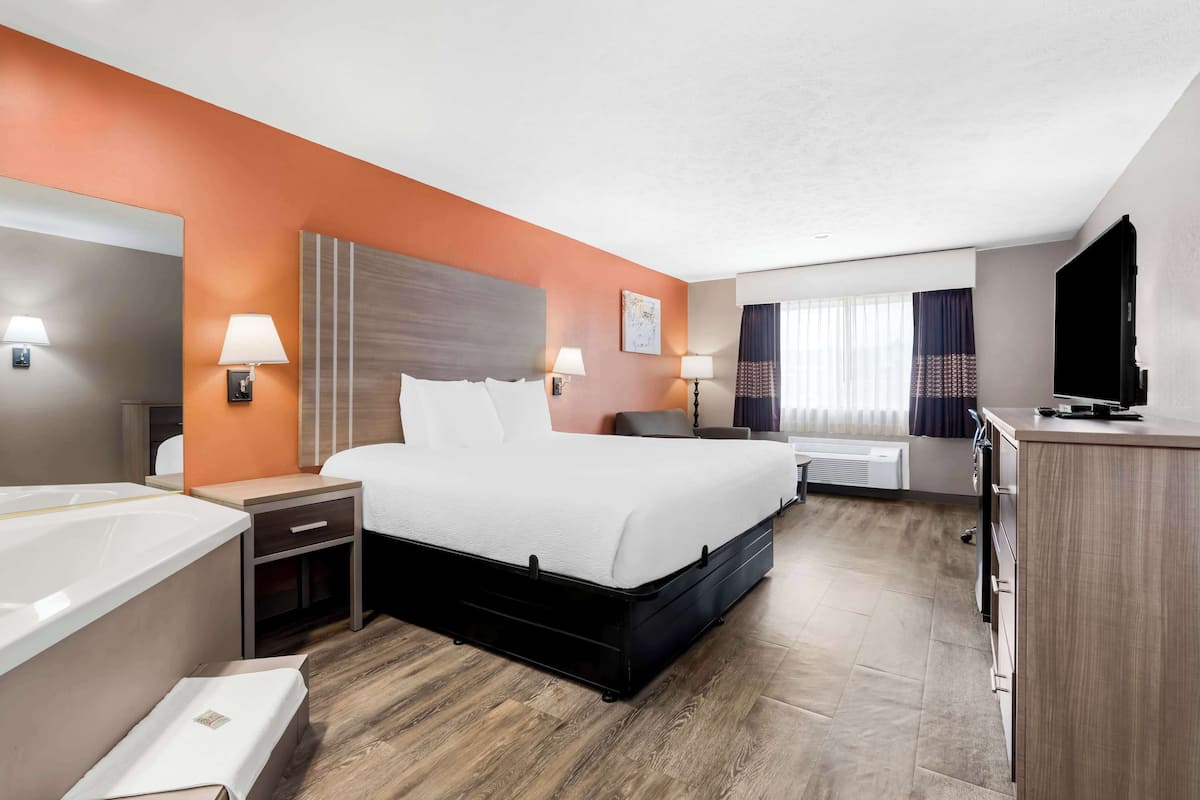 A hotel room with a large bed, bedside tables with lamps, a TV, and a desk area.