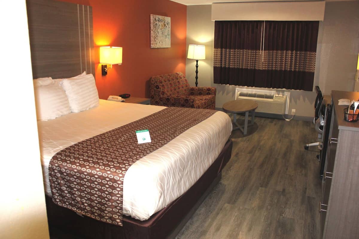 A hotel room with a large bed, two bedside lamps, a chair, a desk, and an air conditioning unit.