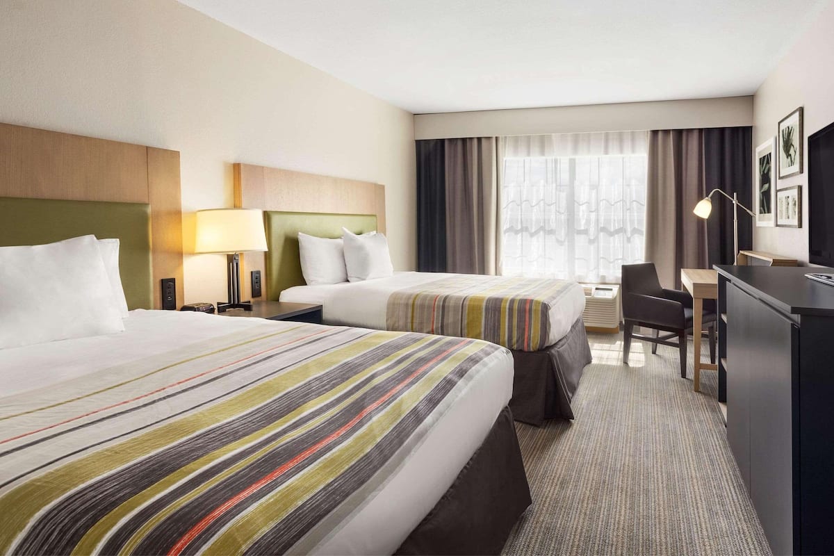A hotel room with two beds, a desk, a chair, and a desk lamp.