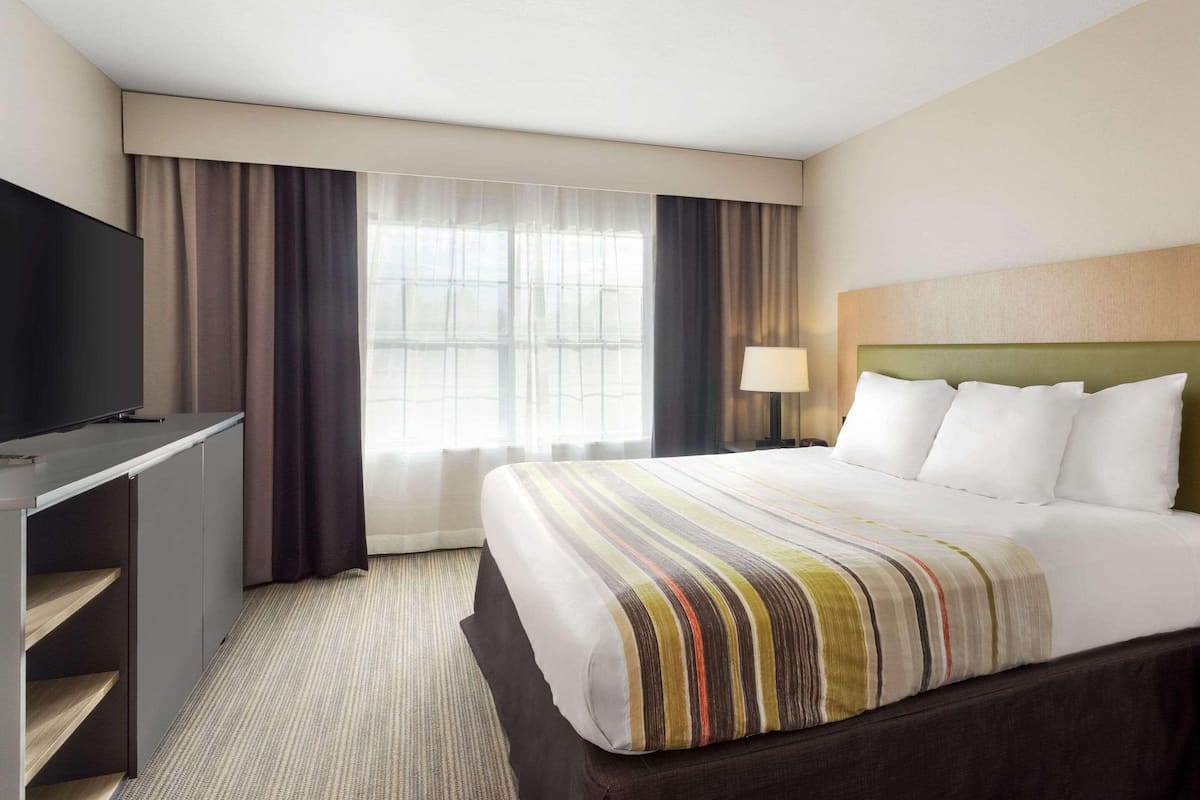 A hotel room with a bed, a TV, a desk, and a window with curtains.
