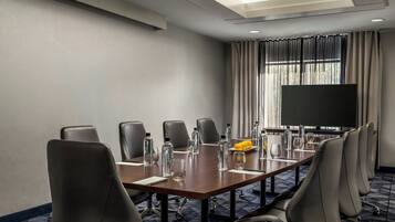 A conference room with a long table, multiple chairs, a large screen, and a window with curtains.