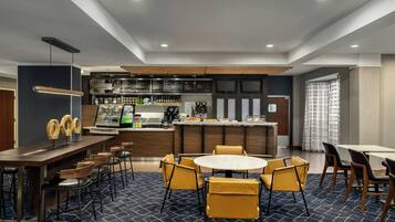 Un moderno vestíbulo de hotel con una zona de bar, áreas de estar y una cocina al fondo.