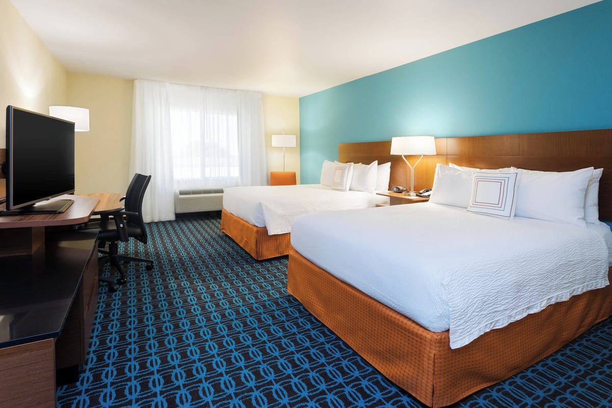 A hotel room with two beds, a desk with a computer, and a TV.