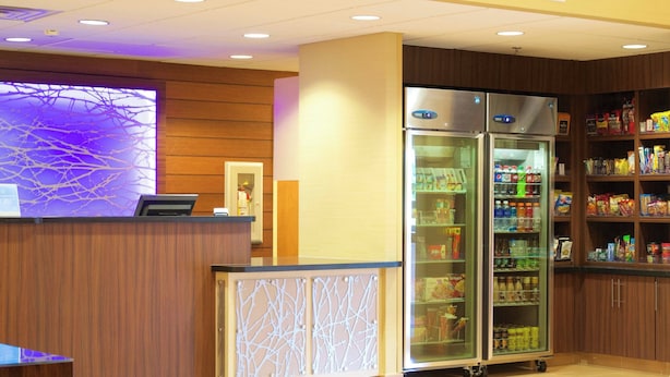 A reception area with a wooden reception desk, two glass-fronted refrigerators stocked with beverages, and a wall with a decorative light fixture. - Fairfield Inn & Suites Odessa (Odessa)