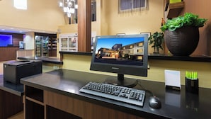 A reception desk with a Lenovo monitor, a desktop computer, and a printer. There is a potted plant on the counter and a wall-mounted shelf with decorative items. - Fairfield Inn & Suites Odessa (Odessa)