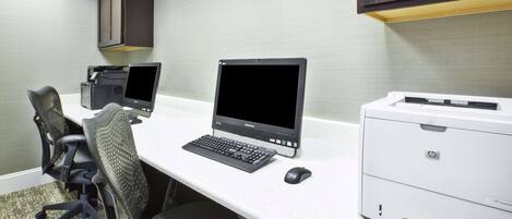 Un espacio de trabajo con dos computadoras de escritorio, una impresora y sillas de oficina.