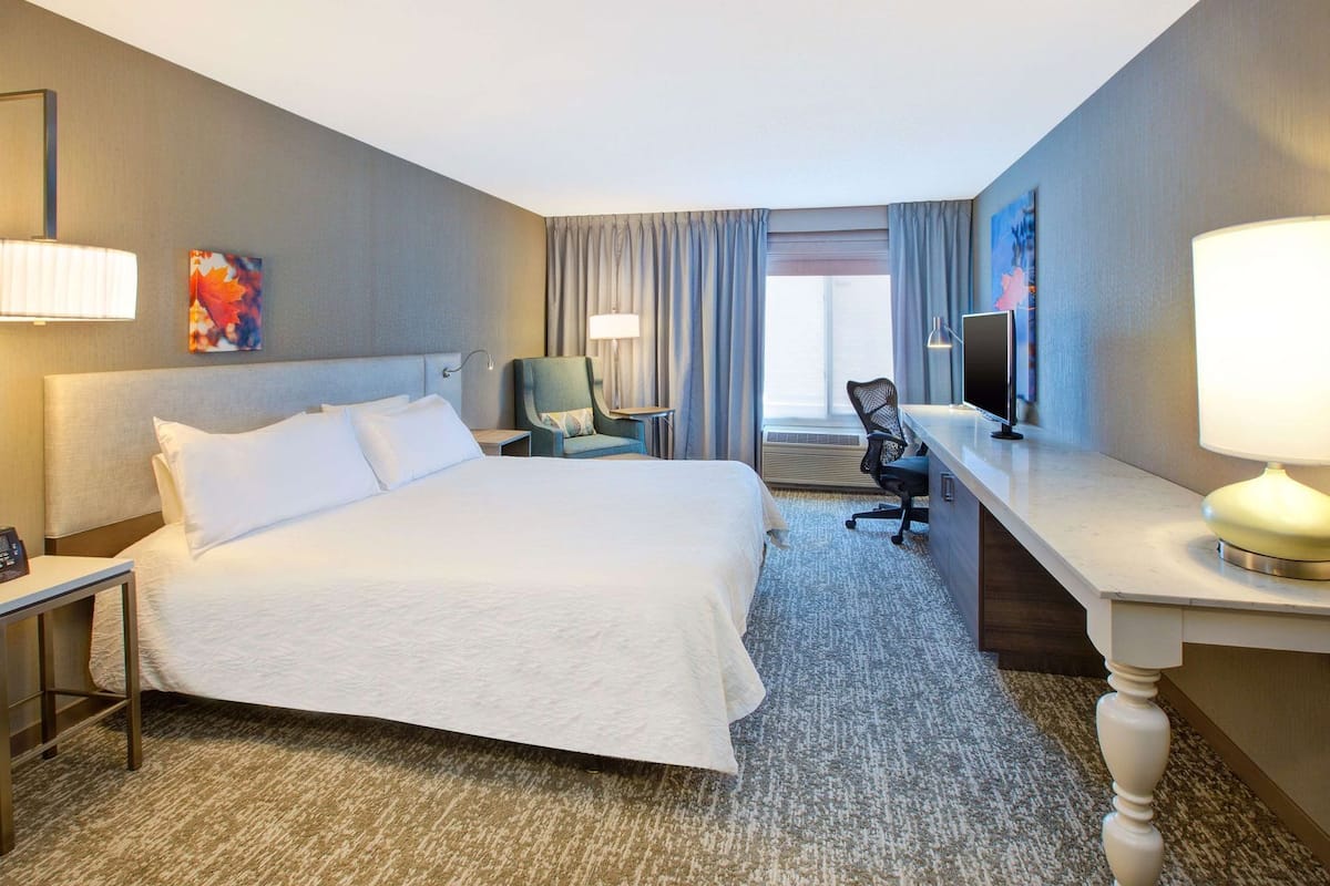 A hotel room with a large bed, a desk with a chair, a TV, and a window with curtains.