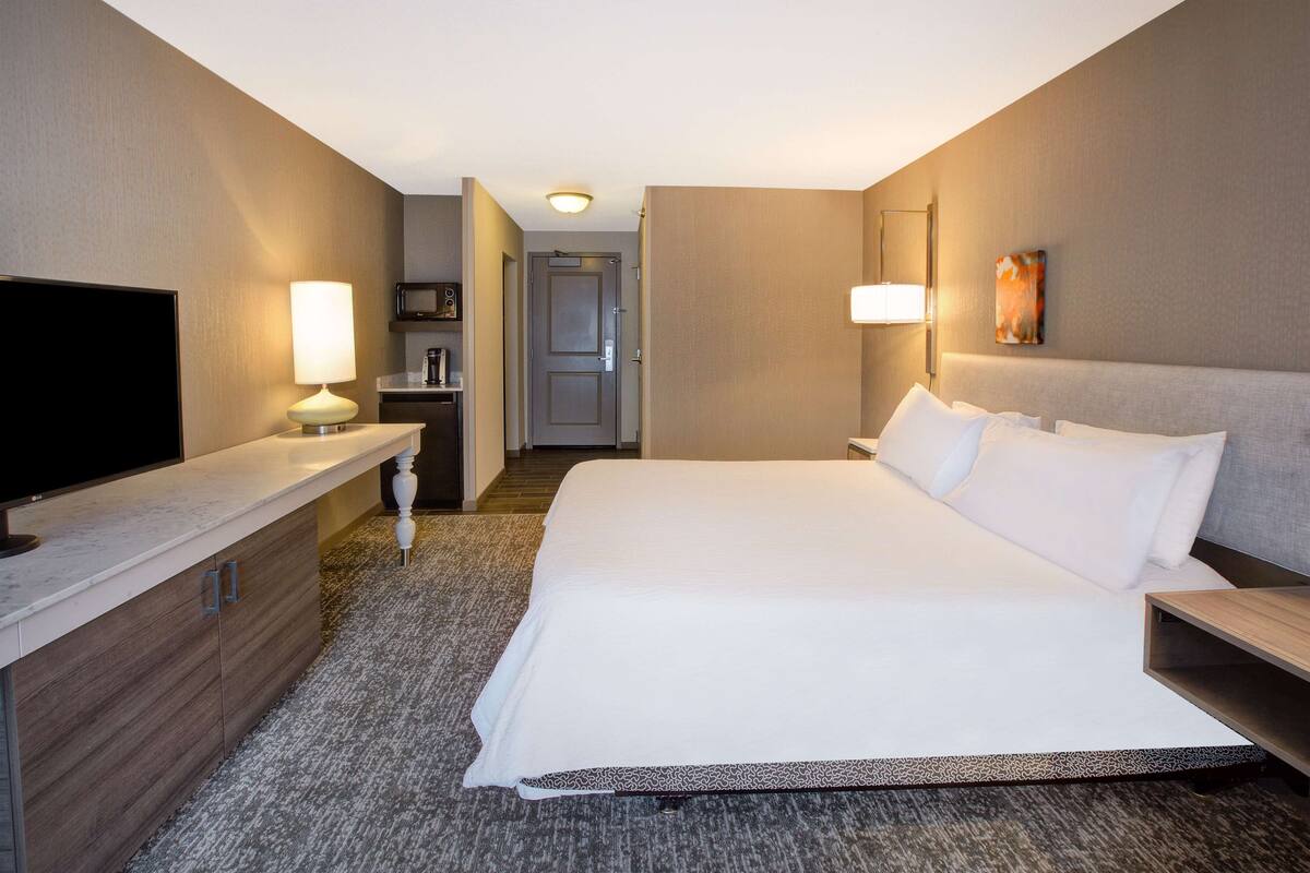 A hotel room with a large bed, a flat-screen TV, a desk with a lamp, and a door leading to a bathroom.