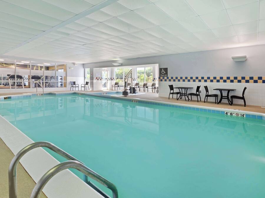 Ein Innenpool mit klarem Wasser, einem Lifter für den Pool und mehreren Tischen und Stühlen rund um den Poolbereich.