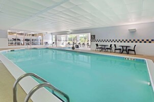 An indoor swimming pool with clear water, a pool lift, and several tables and chairs around the pool area.