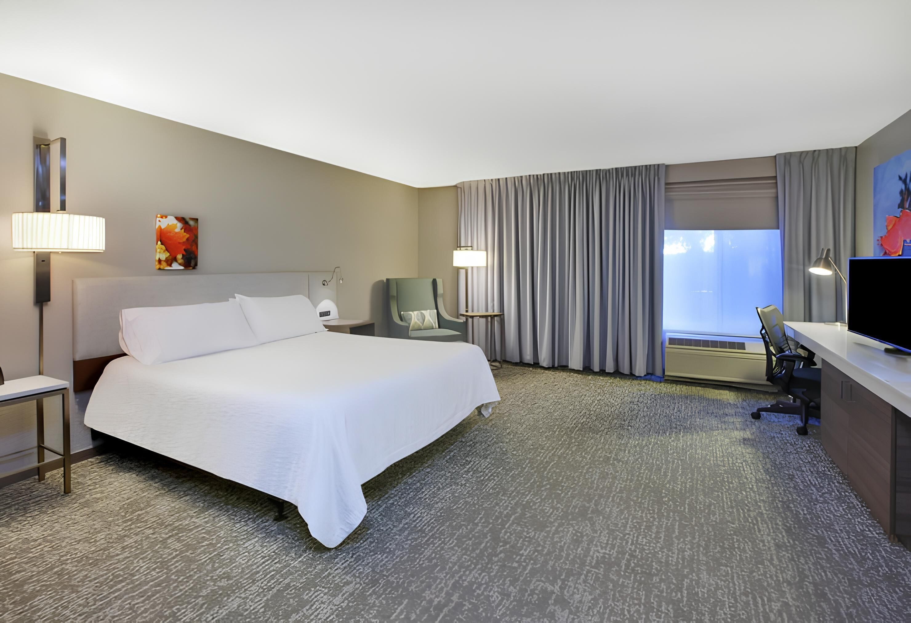 Une chambre d’hôtel avec un grand lit, un bureau équipé d’un ordinateur, une chaise et un téléviseur.