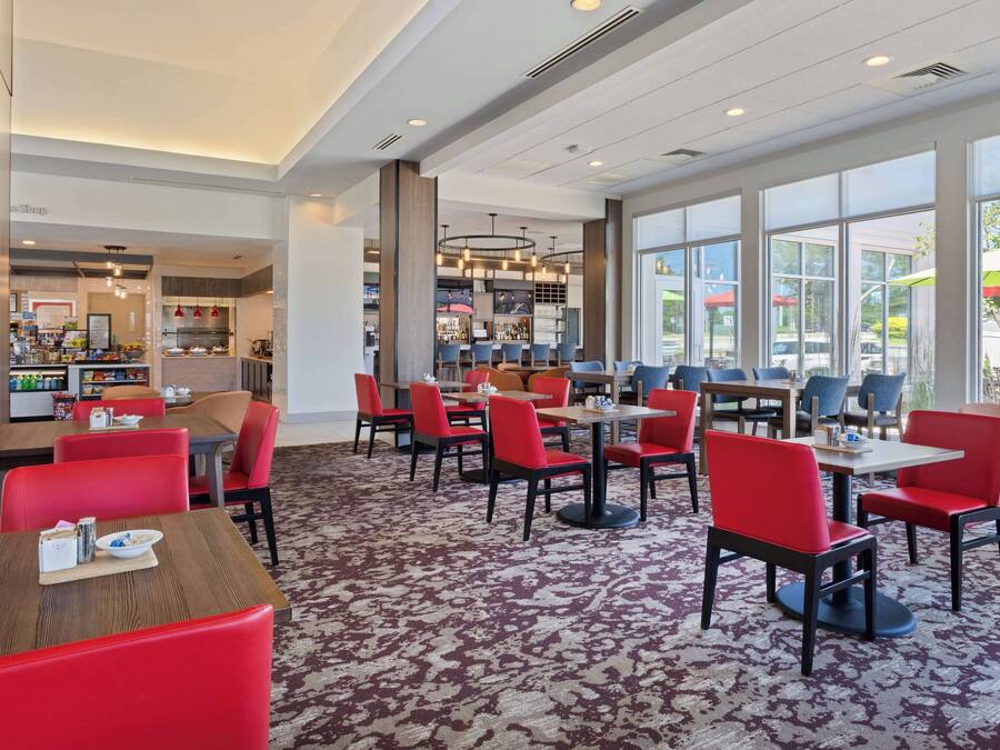 Un restaurante con sillas y mesas rojas, ventanas amplias y piso alfombrado.
